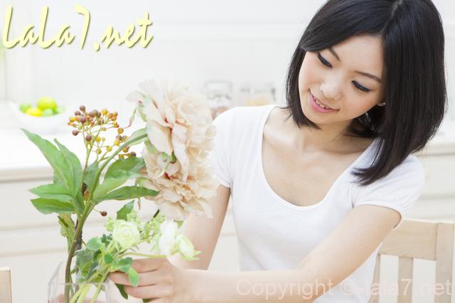 白いTシャツを着た若い女性　花瓶の花を見ている